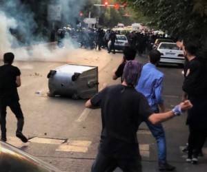 Iranian protestors clash with a line of police in riot gear.